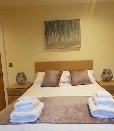A neatly made bed with pillows, a blanket, and folded towels on a textured bedspread.