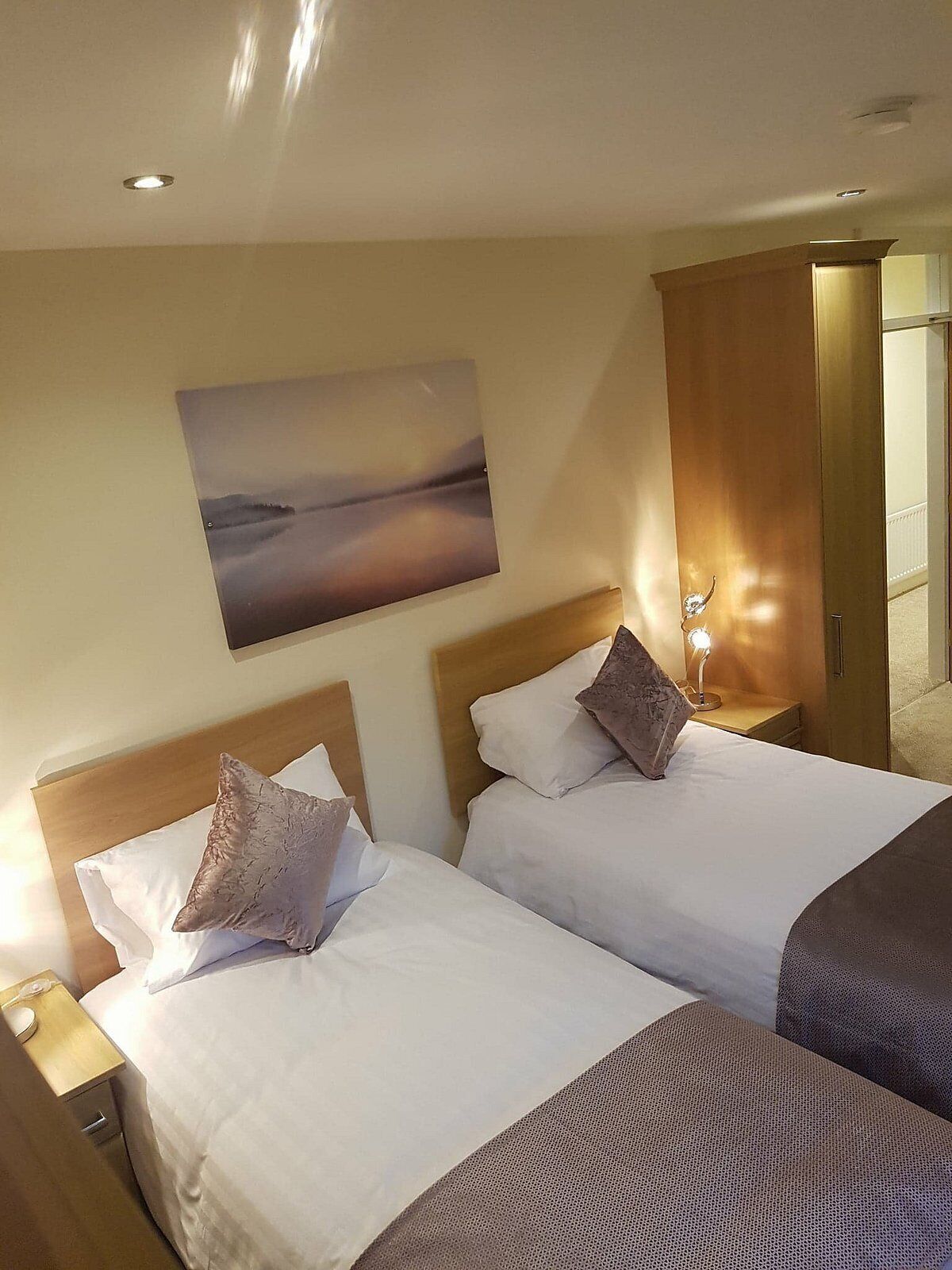 A hotel room with two beds, a painting on the wall, and a door leading to another room.