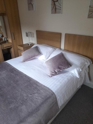A bed with a wooden headboard, two pillows, a bedside table with a lamp, and a grey blanket.