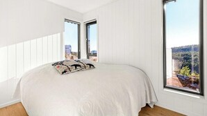 Ein Schlafzimmer mit einem großen Bett, zwei Fenstern und Blick auf ein bewaldetes Gebiet.
