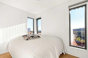 Ein Schlafzimmer mit einem großen Bett, zwei Fenstern und Blick auf ein bewaldetes Gebiet.