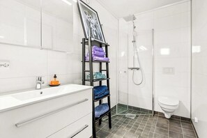 A bathroom with a white sink, a shower, a toilet, and a towel rack with folded towels. - Bird house-inspired cabin near Kragerø (Søndeled)