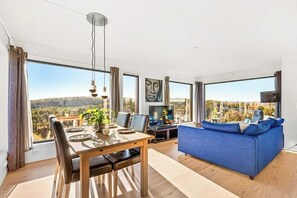 Ein modernes Wohnzimmer mit Essbereich, großen Fenstern und Blick ins Grüne.