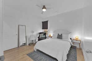 A bedroom with a bed, a ceiling fan, a bedside table with a lamp, a chair, and a mirror. - Olde Walkerville Wonder! (Windsor)