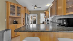 A kitchen with wooden cabinets, a granite countertop, a refrigerator, a microwave, and a ceiling fan. - Olde Walkerville Wonder! (Windsor)