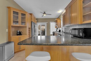 A kitchen with wooden cabinets, a granite countertop, a refrigerator, a microwave, and a ceiling fan. - Olde Walkerville Wonder! (Windsor)