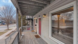 A covered porch with a wooden deck, a red door, and a large window. - Olde Walkerville Wonder! (Windsor)