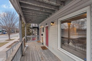 A covered porch with a wooden deck, a red door, and a large window. - Olde Walkerville Wonder! (Windsor)