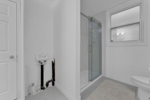 A bathroom with a toilet, a glass shower enclosure, and a white sink. - Olde Walkerville Wonder! (Windsor)