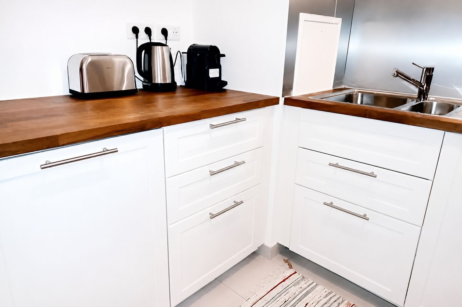 A modern kitchen with white cabinets, a wooden countertop, a sink, and a kettle.