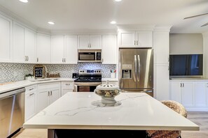 A modern kitchen with white cabinets, stainless steel appliances, a marble island, and a patterned backsplash. - Steps To The Beach + Oceanfront Pool! (Hilton Head Island)