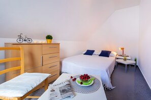 Ein Schlafzimmer mit Bett, Schreibtisch, Stuhl, Kommode und einem kleinen Tisch mit Obstschale.