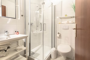 Et moderne badeværelse med en glasafskærmet brusekabine, en hvid vask og et toilet.