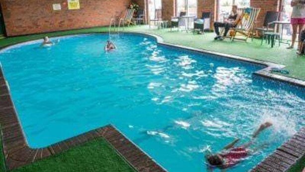 An indoor swimming pool with a brick wall, a diving board, and a grassy area. - Lodge Sleeps 6 With Indoor Pool & Parking (Maen-y-groes)