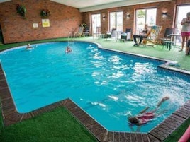 An indoor swimming pool with a brick wall, a diving board, and a grassy area.
