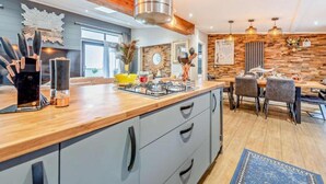 A modern kitchen with a wooden countertop, a gas stove, and a dining area with a table and chairs. - Lodge Sleeps 6 With Indoor Pool & Parking (Maen-y-groes)