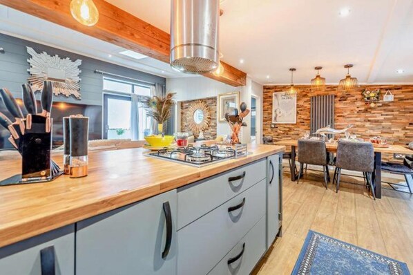 A modern kitchen with a wooden countertop, a gas stove, and a dining area with a table and chairs. - Lodge Sleeps 6 With Indoor Pool & Parking (Maen-y-groes)