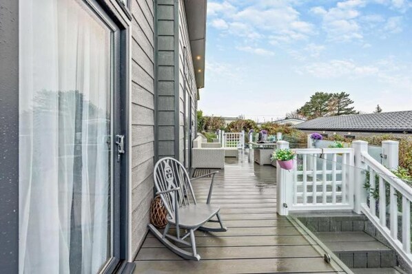 A wooden deck with a white fence, a rocking chair, and potted plants. - Lodge Sleeps 6 With Indoor Pool & Parking (Maen-y-groes)