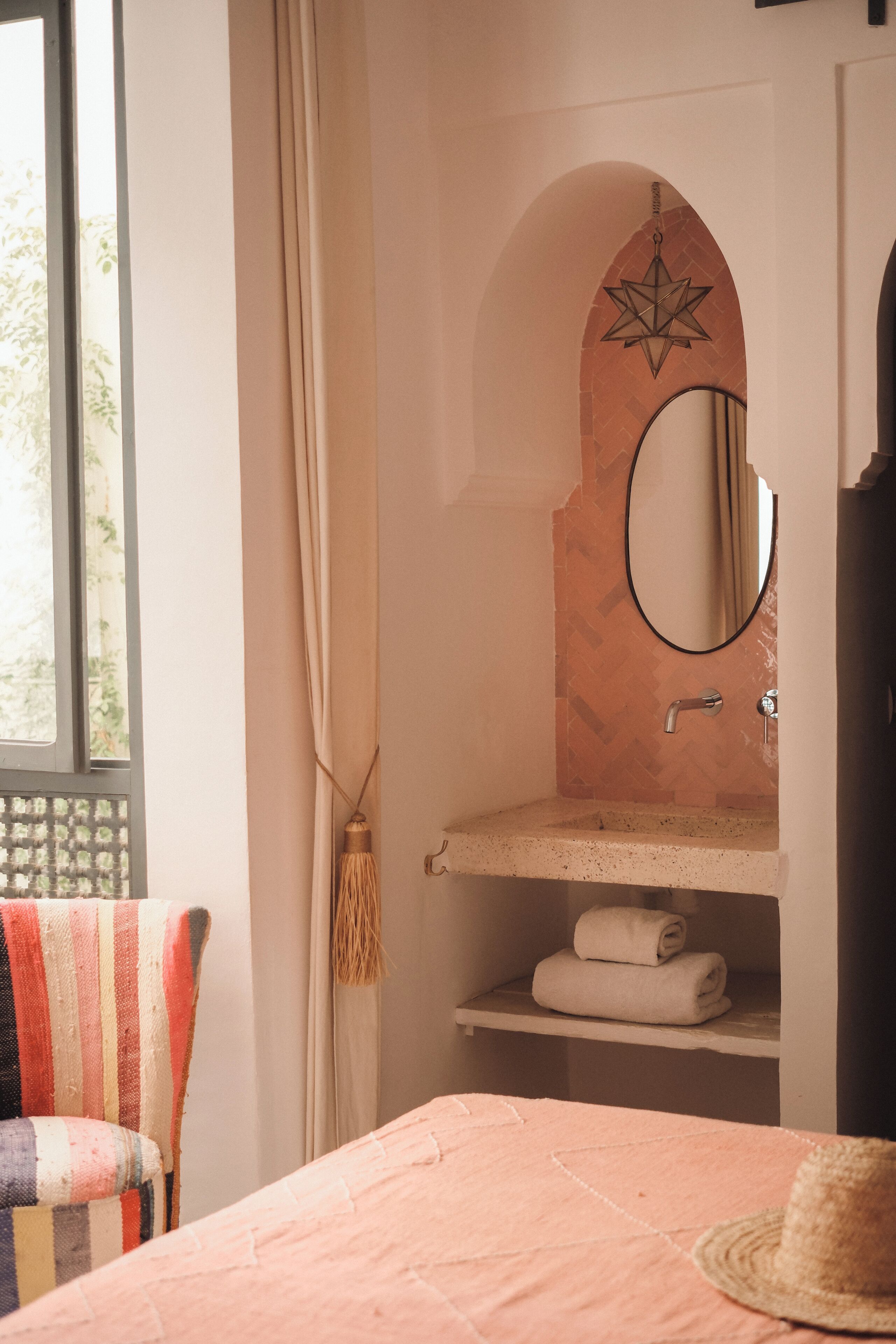 A bathroom with a mirror, towel shelf, and a window with curtains.