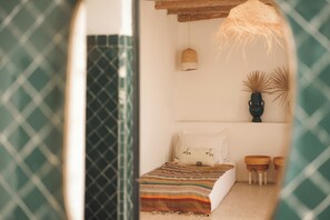 Une chambre à coucher avec un lit, une lampe suspendue, une étagère avec des objets décoratifs et une fenêtre ornée d’un rideau à motifs.