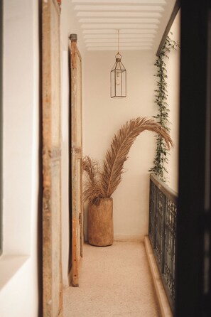 Ein Flur mit Holztürrahmen, einer Hängelampe, einem Blumentopf mit vertrockneten Blättern und einem schwarzen Metallgeländer.