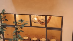 A dining area with a table set for four, surrounded by wicker chairs, and a large window with a view of the outdoors. - Riad le5 - Luxirious private Riad - All Inclusive (Marrakech)