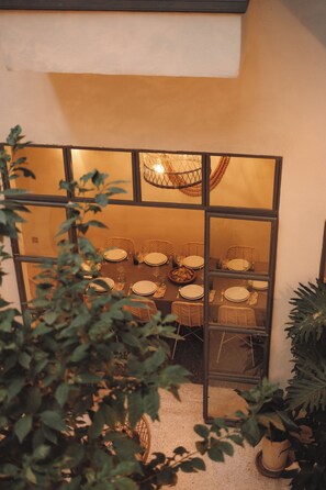 A dining area with a table set for four, surrounded by wicker chairs, and a large window with a view of the outdoors.