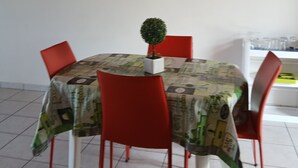 Uma mesa de jantar redonda com toalha de mesa estampada, rodeada por cadeiras vermelhas, um pequeno vaso de planta e um espelho com moldura vermelha na parede.