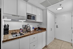 Een moderne keuken met witte kastjes, een granieten aanrecht, een ingebouwde magnetron, een koffiezetapparaat en een spoelbak.