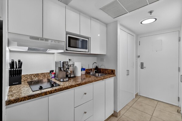 A modern kitchen with white cabinets, a granite countertop, a built-in microwave, a coffee maker, and a sink. - Stylish Ocean view/front Studio + Pool (Sunny Isles Beach)