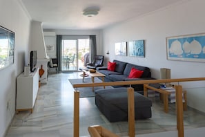 Ein modernes Wohnzimmer mit einer Couch, Hocker und einem Essbereich mit Tisch und Stühlen.