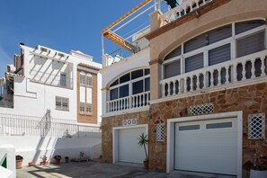 Ein zweistöckiges Gebäude mit Natursteinfassade, weißen Garagentüren und einem Balkon mit Geländer.