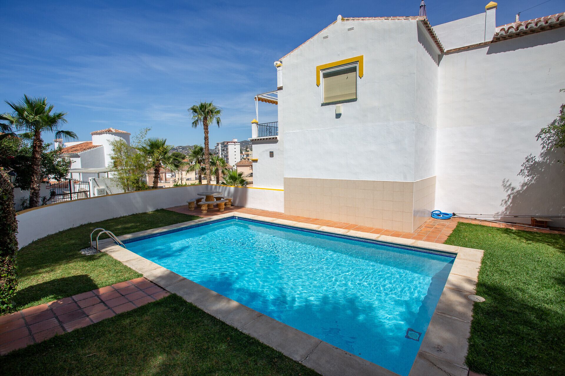 Una piscina con agua cristalina azul, rodeada por un césped bien cuidado y un edificio blanco con un ventanal amarillo.