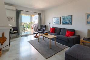 Ein modernes Wohnzimmer mit grauem Sofa, roten Kissen, einem Holztisch und einem Balkon mit Blick.