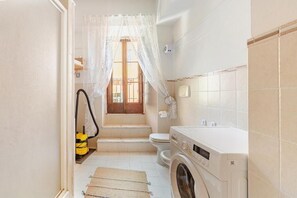 A compact bathroom with a washing machine, toilet, and a window with a curtain. - BQA San Crisogono Apartments Rome-Trastevere (Roma)