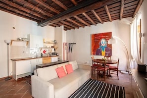 A compact living space with a kitchenette, a sofa with cushions, a dining table with chairs, and a large painting on the wall. - BQA San Crisogono Apartments Rome-Trastevere (Roma)