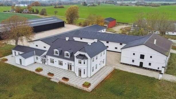 A large, white, multi-story building with a symmetrical facade, a covered driveway, and a surrounding green landscape. - Estate in Calm Nature (Soro)