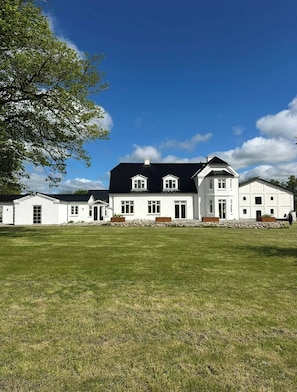 A large, white building with a black roof, multiple windows, and a well-maintained lawn. - Estate in Calm Nature (Soro)
