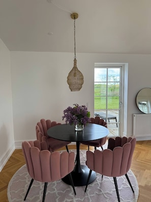 A dining area with a round table, pink chairs, a hanging light fixture, and a view through a glass door. - Estate in Calm Nature (Soro)