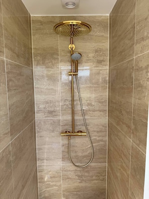 Une douche avec un revêtement doré, une douchette à main et un panneau de commande fixé au mur.