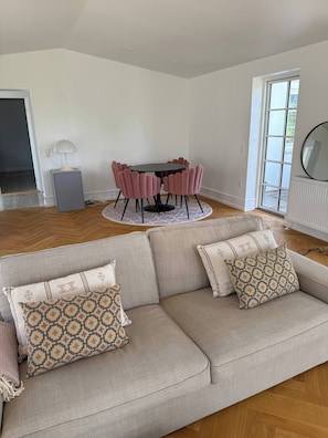 A living room with a sofa, patterned cushions, a round table with chairs, and a lamp.