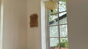 A room with a large window, a hanging light fixture, and a Buddha statue on the floor. - Estate in Calm Nature (Soro)