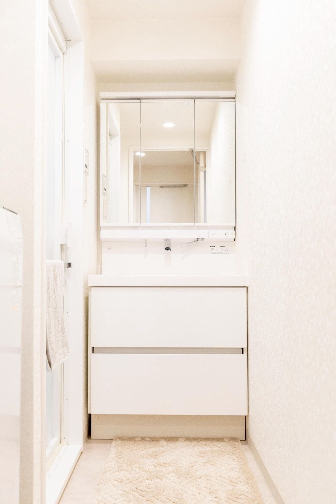 A narrow hallway with a white door, a white countertop, and a mirror above it.