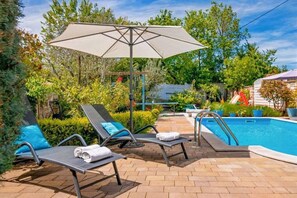 Een zwembadgedeelte met ligbedden, een zwembad en een pergola met een zonnescherm.