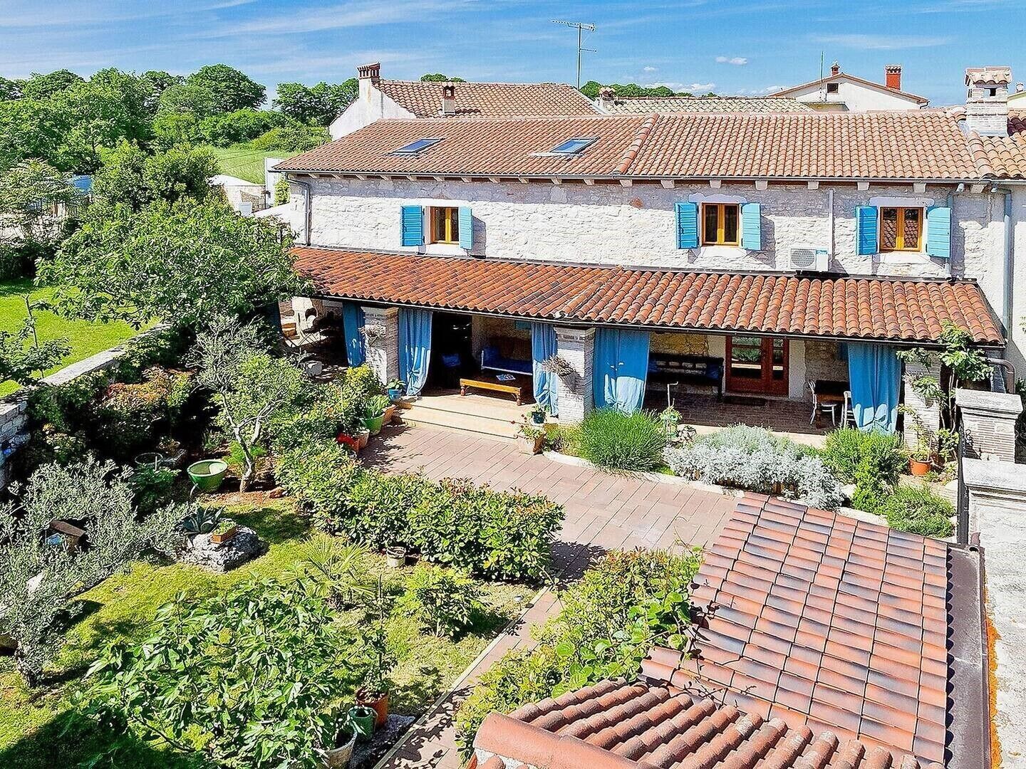 A two-story house with a tiled roof, a covered patio, and a garden.
