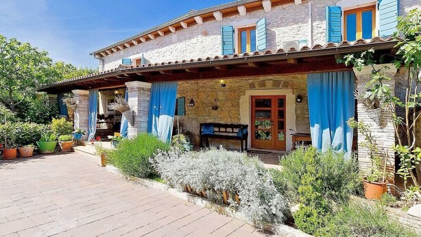 Ein rustikales Steinhaus mit einer überdachten Veranda, Blumentöpfen und einer kleinen Sitzgelegenheit im Freien.