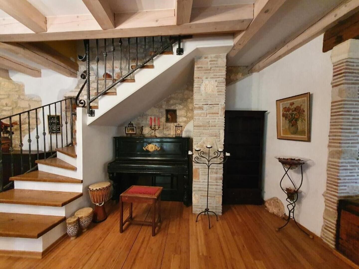 Una scala con gradini in legno e ringhiera in metallo, un pianoforte, un tamburo e un candelabro su un pavimento in legno.
