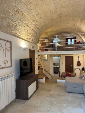 Un vaste espace de vie doté d’un plafond en pierre, d’un téléviseur, d’un escalier et d’un balcon.