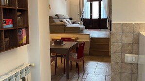 Ein kompakter Wohnbereich mit Essplatz, einer Couch, einer Küchenzeile und Blick durch einen offenen Durchgang.