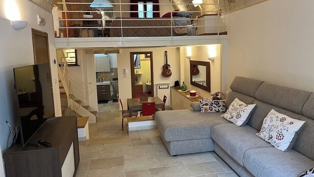 Ein geräumiger Wohnbereich mit einer Couch, einem Fernseher, einer Treppe zu einer oberen Ebene und einer Küche im Hintergrund.